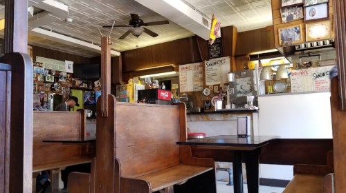 A cozy diner interior with wooden booths, a counter, and vintage decor, featuring a menu and drinks on display.