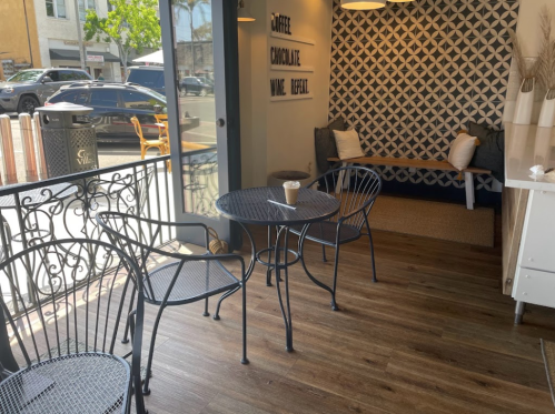 Cozy café interior with black metal chairs, a small table, and a decorative wall, featuring a coffee cup on the table.