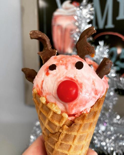 A festive ice cream cone shaped like a reindeer, with a red nose, chocolate antlers, and a cheerful expression.