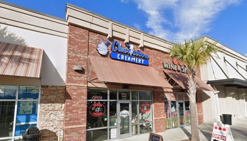 Exterior of Charleston Creamery with a sign, awnings, and palm trees under a blue sky. Nearby wine shop visible.