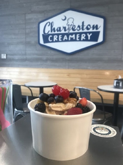 A cup of frozen yogurt topped with berries and a cherry, with a creamery sign in the background.