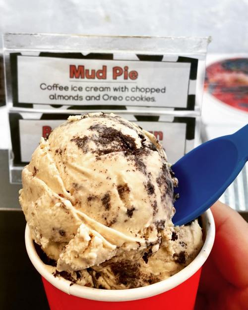 A scoop of coffee ice cream with chopped almonds and Oreo cookies in a red cup, with a blue spoon.