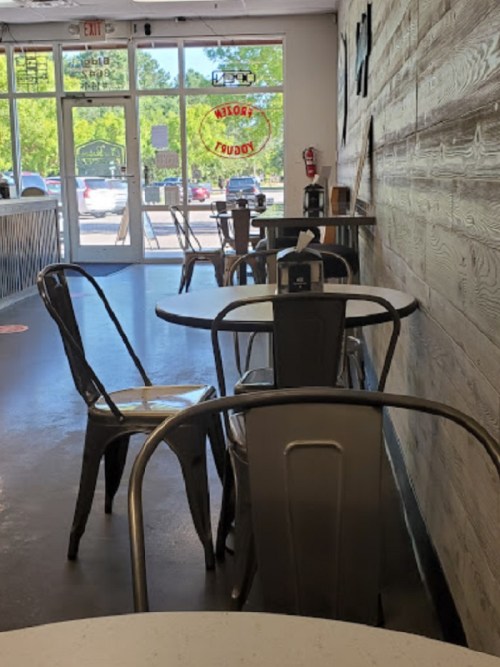 A cozy café interior with empty tables and chairs, featuring wooden walls and large windows letting in natural light.