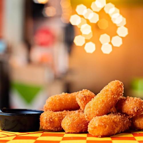 A stack of golden, crispy cheese sticks next to a small bowl of dipping sauce, with a blurred background.