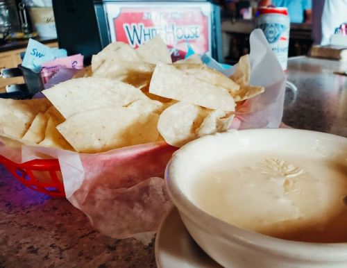 A basket of tortilla chips next to a bowl of creamy dip on a restaurant table.