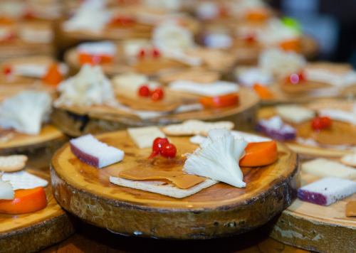 A close-up of wooden platters topped with assorted cheeses, crackers, and garnishes like red berries and vegetables.