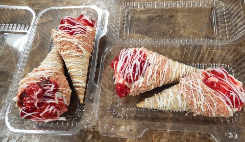 Two dessert cones with cherry topping and drizzled white icing, displayed in clear plastic containers.