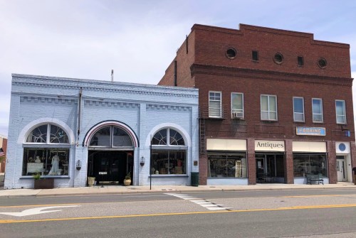 Two historic buildings side by side, one blue with arches and the other red brick, featuring shops and antique displays.