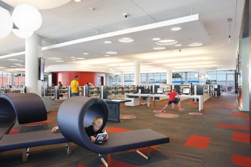 A modern library interior with children reading and playing, featuring unique seating and bright, open spaces.