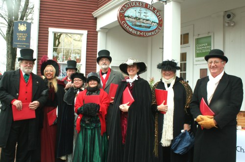 A group of people in Victorian costumes, holding red folders, stand outside the Nantucket Island Chamber of Commerce.