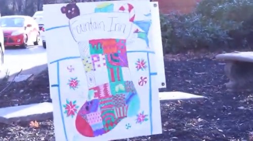 Colorful hand-drawn sign of a decorated Christmas stocking with the text "Fountain Inn" on it, surrounded by greenery.