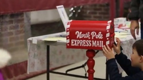 A child placing a letter into a red North Pole Express Mail mailbox at a festive event.