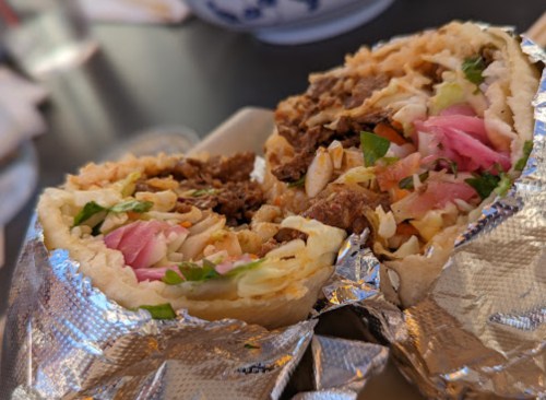 A close-up of a burrito cut in half, revealing layers of meat, rice, vegetables, and wrapped in foil.