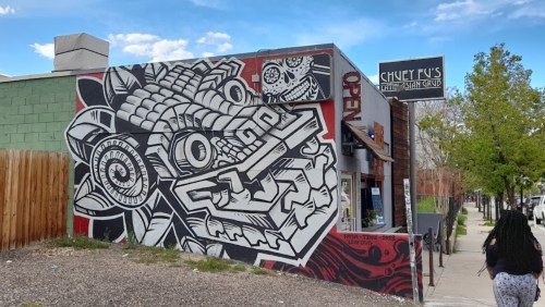 Colorful mural of a dragon on the side of a building, with a person walking by in the foreground.