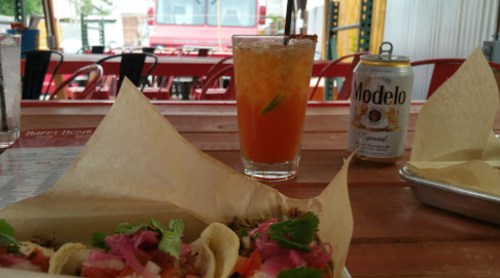 A table with tacos, a cocktail, and a can of Modelo beer in a casual dining setting.