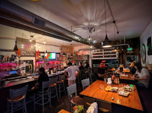 A lively bar scene with patrons at the counter, colorful lights, and a variety of drinks on display.