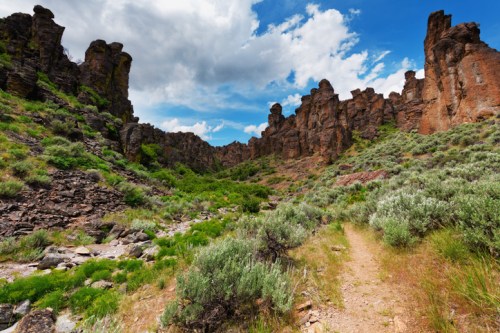 A scenic valley with towering rock formations, lush greenery, and a clear blue sky with scattered clouds.