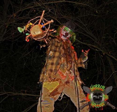 A creepy clown in tattered clothes holds a twisted object, surrounded by dark trees, with "Horror in the Hollow" logo.