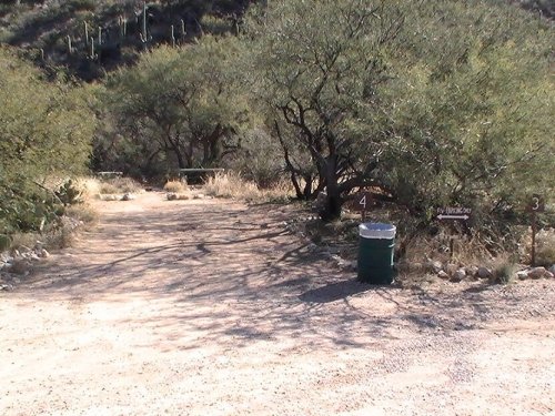 A dirt path leads into a desert area with sparse vegetation and a trash can near trail markers numbered 3 and 4.