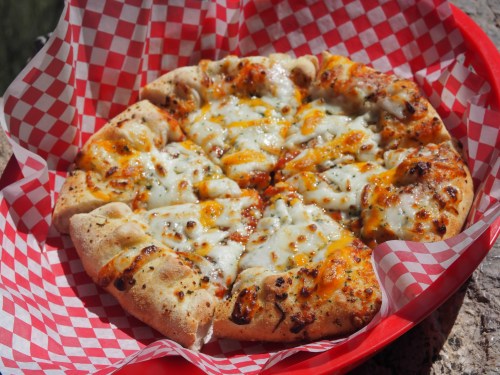 A freshly baked pizza with melted cheese, served in a red basket lined with checkered paper.
