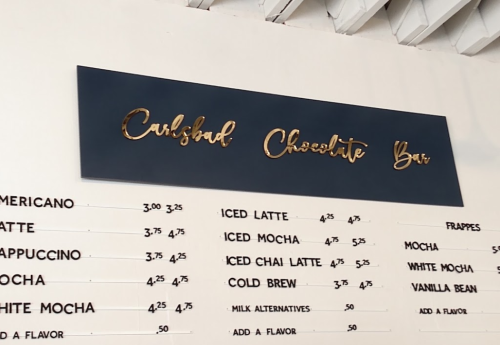 Sign for "Cushbad Chocolate Bar" with a menu listing various coffee and chocolate drink options and prices.