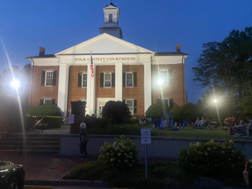 Polk County Courthouse at dusk, with people gathered outside and lights illuminating the building.