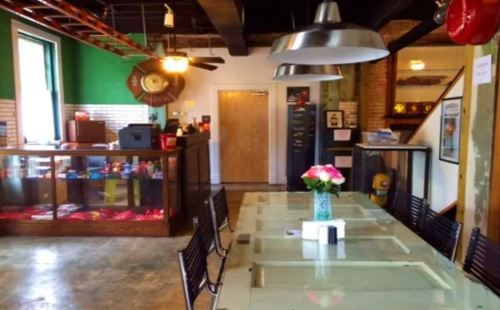 A cozy café interior featuring a glass table, black chairs, and a counter with snacks, decorated with flowers.