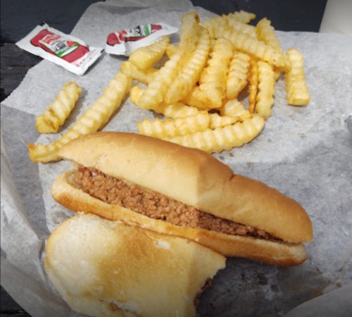 A plate with a hot dog topped with meat and crinkle-cut fries, accompanied by two ketchup packets.