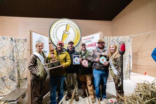 A group of five people in camouflage and formal attire holding awards at a hunting competition event.