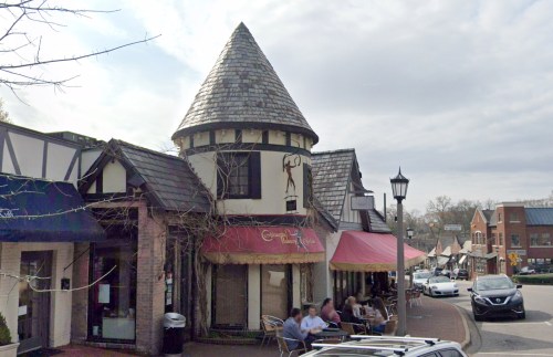 Charming street view featuring a turreted building and outdoor dining, with shops and cloudy skies in the background.