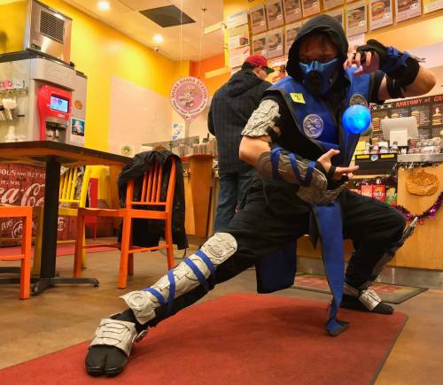 A person in a blue ninja costume poses dramatically in a colorful restaurant, holding a glowing orb.