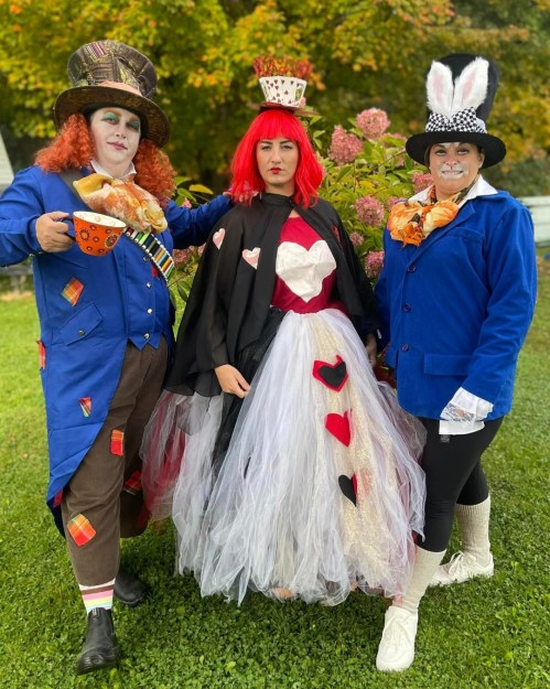 Three people in whimsical costumes: a Mad Hatter, a Queen of Hearts, and a White Rabbit, posing in a colorful outdoor setting.