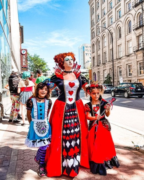 A woman dressed as the Queen of Hearts stands with two girls in costume on a city street.