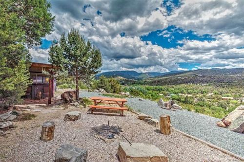 A scenic outdoor area with a picnic table, fire pit, and mountains under a cloudy sky.