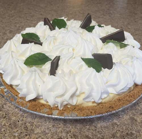 A creamy pie topped with whipped cream, chocolate pieces, and mint leaves, in a graham cracker crust.