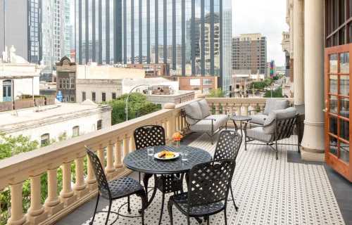 A balcony with a round table and chairs, overlooking a cityscape with tall buildings and greenery.