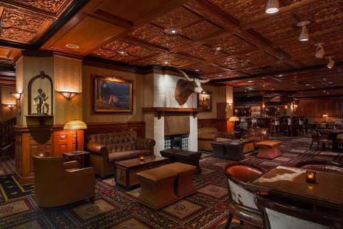 Cozy, upscale lounge with leather seating, wooden accents, and a warm ambiance, featuring a fireplace and artwork.