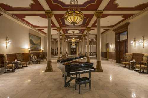 A grand piano in a spacious, elegantly decorated lobby with chandeliers and marble flooring.