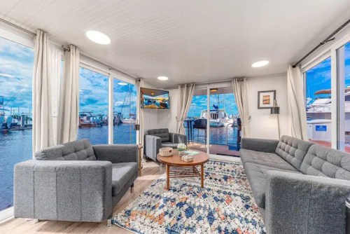 Cozy living area with gray sofas, a coffee table, and large windows overlooking a marina with boats.