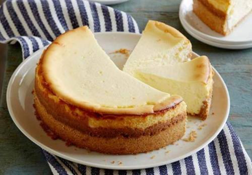 A creamy cheesecake on a plate, with a slice cut out, resting on a striped cloth.