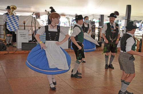 A group of people in traditional Bavarian attire dancing on a wooden floor at a festive event.