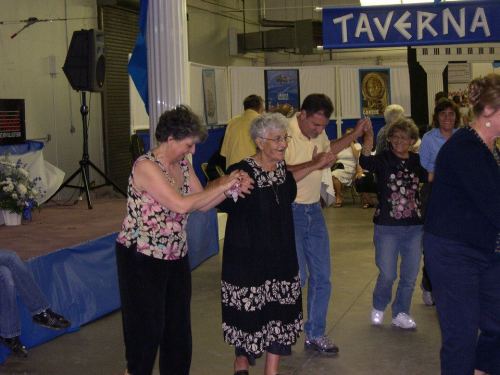 A group of people dancing together at an event, with a stage and decorations in the background.
