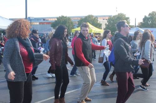 A group of people dancing together outdoors at a festive event, wearing casual clothing and smiling.