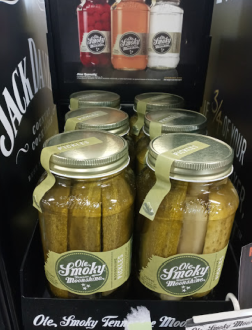 Jars of pickles labeled "Ole Smoky Moonshine" displayed on a shelf, with various flavors visible.