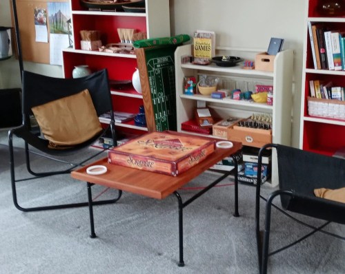 A cozy game area with two chairs, a low table, and shelves filled with board games and colorful items.