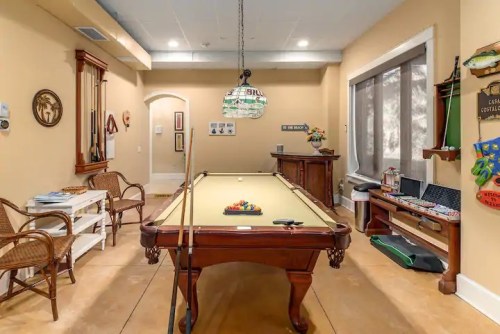 A cozy game room featuring a pool table, wicker chairs, and decorative wall art in warm tones.
