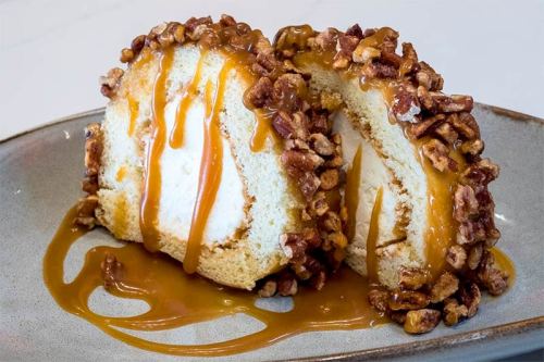 A slice of dessert with creamy filling, topped with caramel sauce and crushed nuts, served on a gray plate.