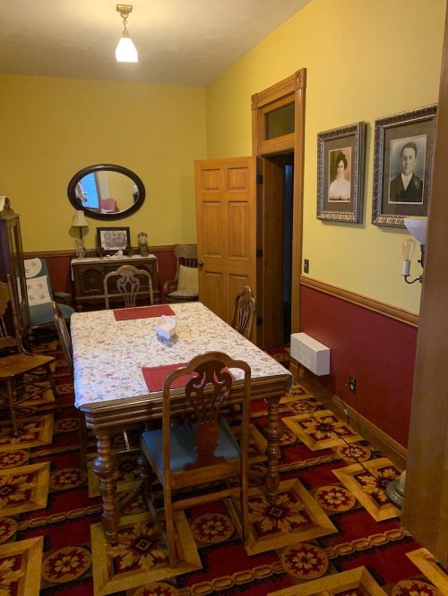 A vintage dining room with a patterned carpet, wooden furniture, and framed portraits on the walls.