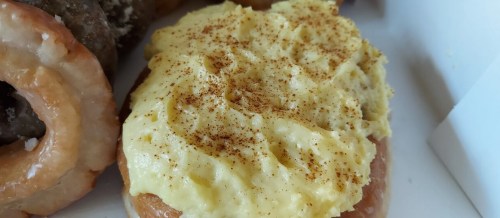A close-up of a donut topped with a creamy yellow frosting and a sprinkle of cinnamon.
