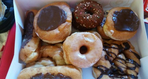 A box of assorted donuts, including chocolate-covered, glazed, and a sprinkled donut.